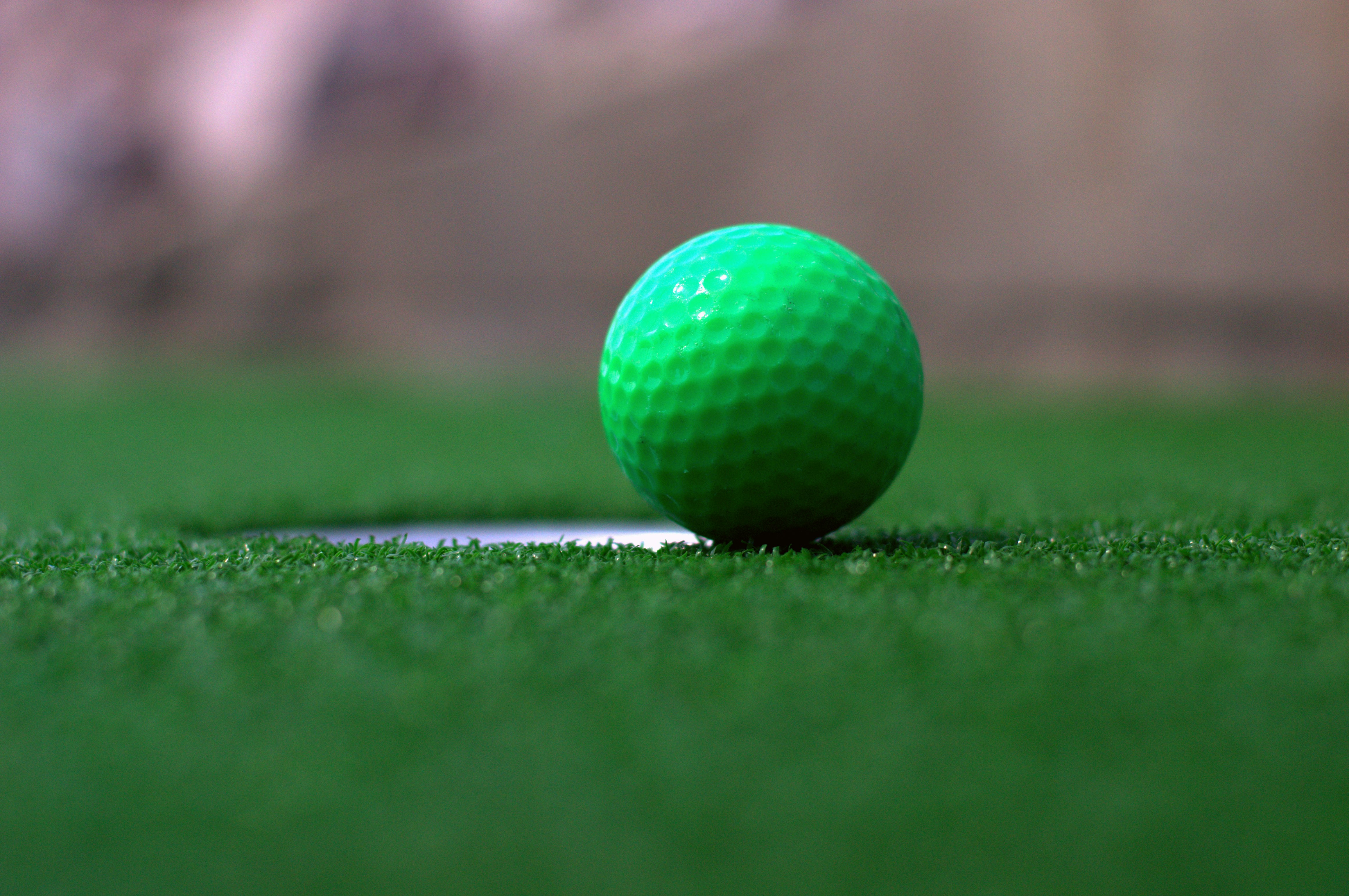 Bright green golf ball resting at the edge of a hole on premium artificial turf