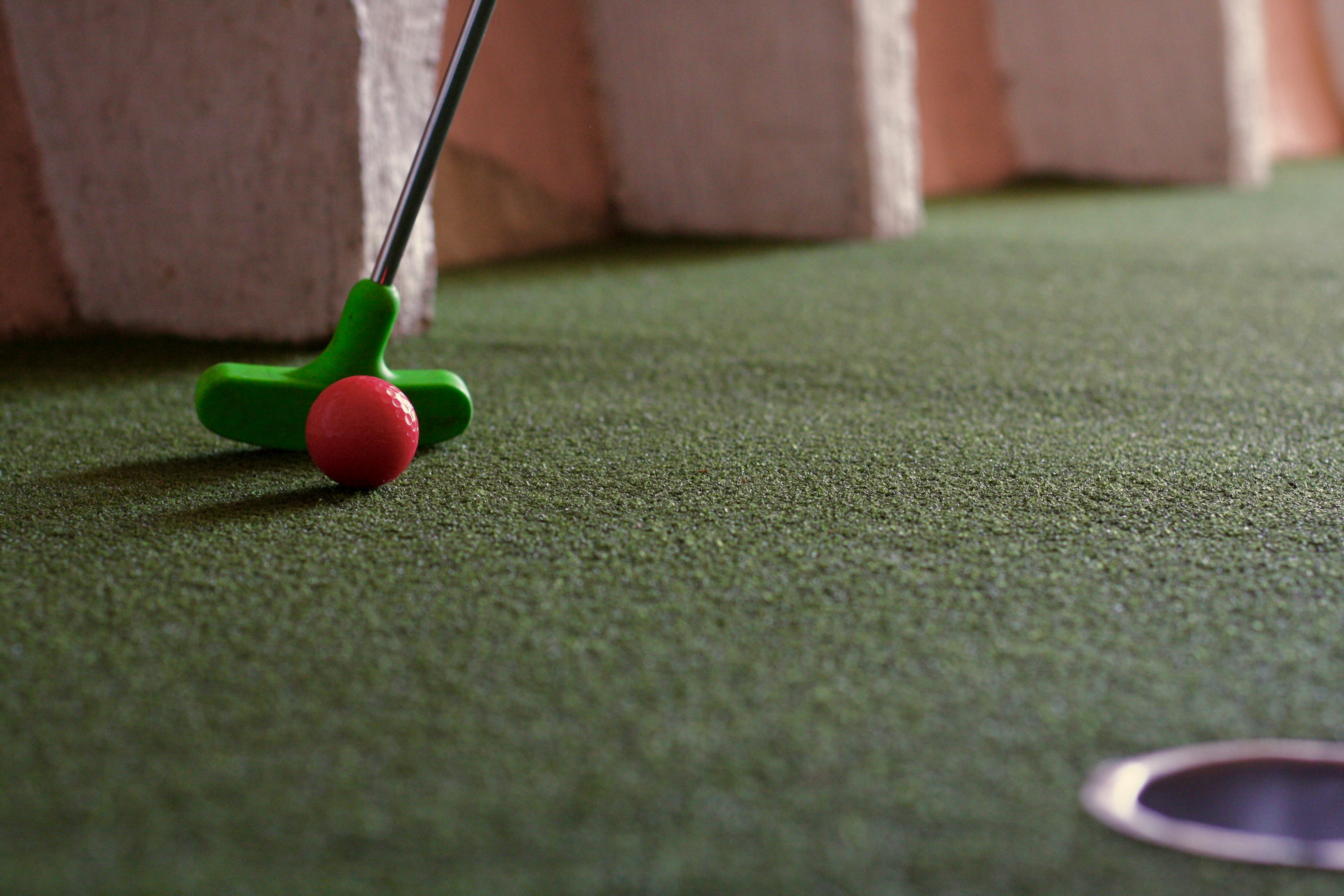 Green putter and pink ball on a mini golf course green next to the hole